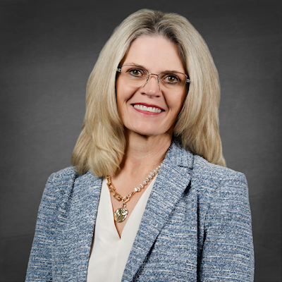 Headshot of District Clerk Marci Gilbert, a Caucasian female with blonde hair and glasses, wearing a cream blouse, necklace, and blue and white business jacket.