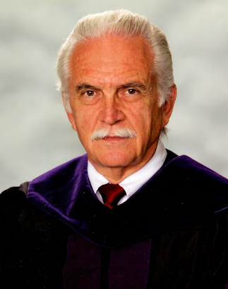 Headshot of Carroll Johnson, a white male with white hair and a moustache; he wears a purple robe, with a white button-up, and a red tie.